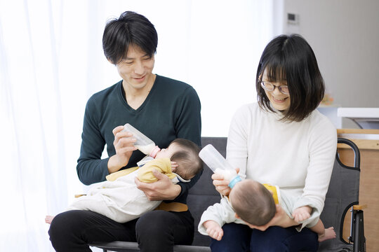 双子の赤ちゃんのミルクをあげるアジア人の両親