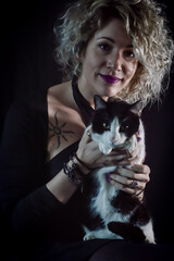 Portrait of a beautiful curly and smiling blonde woman holding a black and white cat