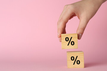 Woman stacking wooden cubes with percent signs on light pink background, closeup. Space for text