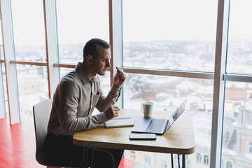 Smart young man looking for information on a website and working as a freelancer on developing a graphic project on a modern laptop using a wireless internet connection in a cafe interior