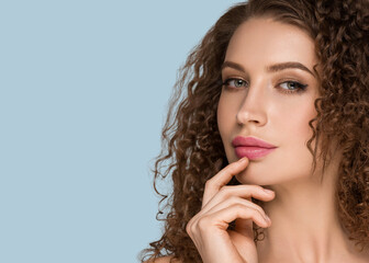 Curly long brunette hair woman touching face beauty close up female portrait. Color backgound blue