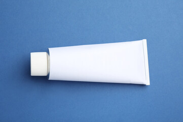 Blank white tube of ointment on blue background, top view. Space for text