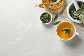 Sage tea and green leaves on light grey marble table, flat lay. Space for text