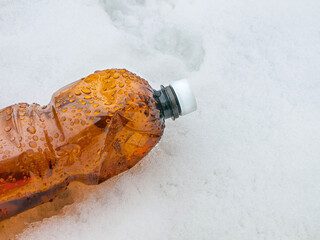 Plastic brown bottle with a white stopper in the snow, garbage in nature