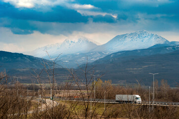 Side view of the spectacular mountains and truck on the road. A truck on the road passes under the snowy mountain peaks