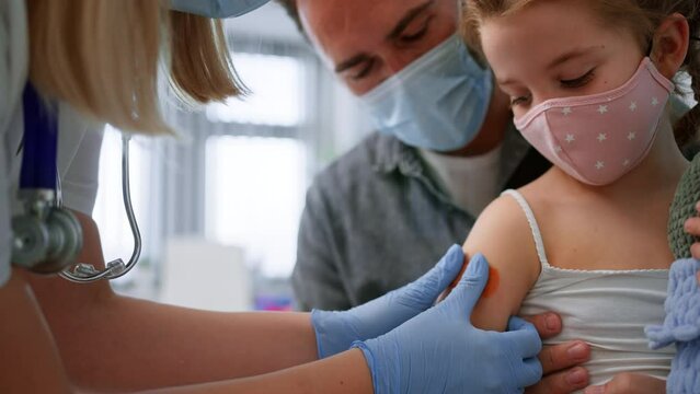 Little girl sitting on fahter's lap and getting vaccinated in doctor's office
