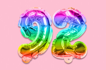 Rainbow foil balloon number, digit ninety two on a pink background. Birthday greeting card with inscription 92. Top view. Numerical digit. Celebration event, template.
