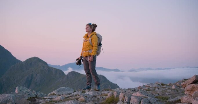Cinematic sunset shot of young woman adventurer on evening midnight sun hike shoot content on professional photo camera. Travel blogger or influencer explore world. Concept female traveller wanderlust
