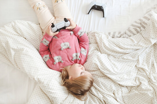 Little cute girl playing with joystick in bed at home.