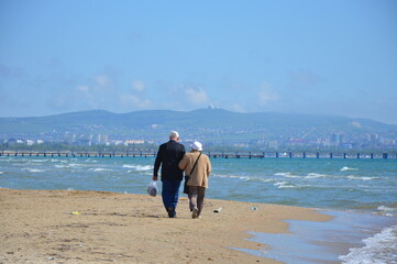 Elderly couple walks on the sand beach. Senior couple on a stroll at sandy coastline. Romance. Senior. Love. Together. Two. Elder generation. Togetherness