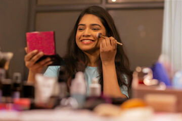 Young woman doing her make up in front of mirror