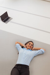 Young business woman in formal outfit lying on floor with hands behind neck