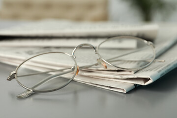 Newspapers and glasses on grey table, closeup