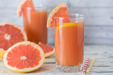 Grapefruit juice and ripe grapefruits on a light wooden background