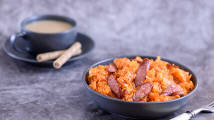 Stewed cabbage with sausages in black plate. horizontal side view