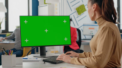 Company worker using isolated green screen on monitor with chroma key. Business woman looking at computer with mock up template and background in startup office. Mock-up copy space