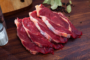 Sliced beef pieces on dark wooden board with laurel leafs and peas of bitter pepper