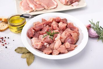 Diced meat on a white plate. Composition with raw poultry, pork meat in cubes and seasonings, on white background.