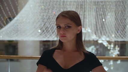 Caucasian girl gestures ok sign. A beautiful European woman in a black dress on a background of a large crystal chandelier. Portrait of a pretty lady.