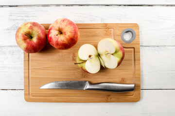 Cut red apple and stainless steel knife on a bamboo cutting board