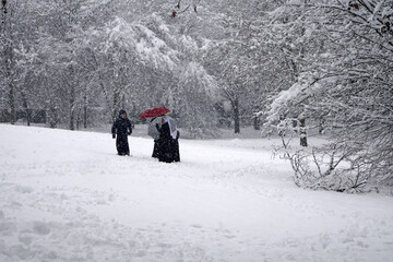 Gruppo di suore con ombrello cammina nel paesaggio innevato durante la nevicata ai margini del bosco 