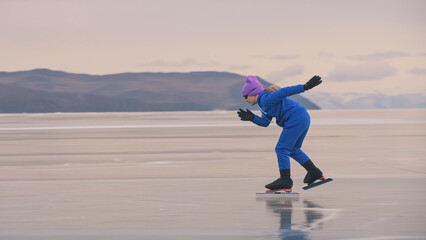The child train on ice professional speed skating. The girl skates in the winter in sportswear, sport glasses, suit. Children speed skating short long track, kid sport. Outdoor slow motion.