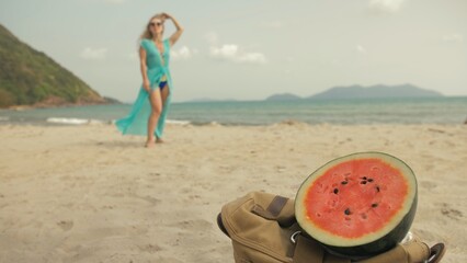 The cheerful woman in blur, against the background of a watermelon on tropical sand beach sea. Portrait attractive beautiful girl caucasian spend summer weekend in outdoor. White shirt beachwear.