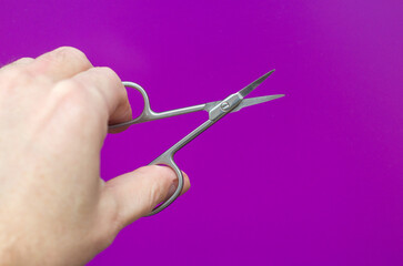 A man holds in his hand small scissors for manicure on a purple background