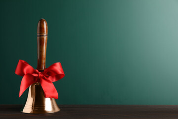 Golden bell with red bow on wooden table near green chalkboard, space for text. School days
