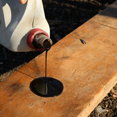 pouring brown technical oil from a white plastic canister onto a wide board, treating a wooden...