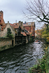 Fototapeta na wymiar Bruges water canal with the typical image of its little houses, with a boat sailing through the canal. Cloudy day.
