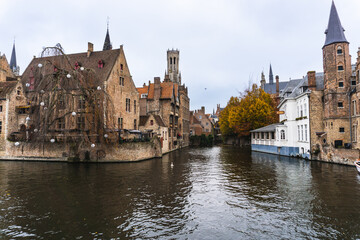 Fototapeta na wymiar Panorama of Bruges, where there is a water channel, at the bottom of the image the church tower and typical Belgian houses. Cloudy day with autumn colors.