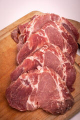 Pork meat cut into chops, slices, on a wooden chopping board, on a white. Raw pork neck steaks, cutlets, close up.