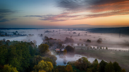 Foggy field with forest before dawn from a bird's-eye view. Clear and gloomy pink-purple sky.