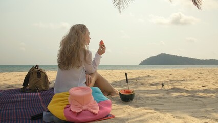 The cheerful woman holding and eating slices of watermelon on tropical sand beach sea. Portrait...