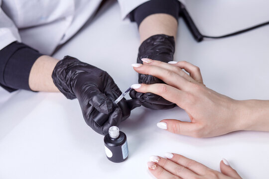 Partial view of manicurist in latex black gloves applying nail polish while making manicure to client on blurred foreground. Fine brush manicure nail polish, modeling gel.