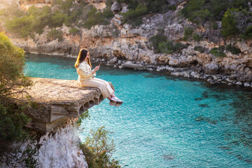 Woman sitting on a cliff using her phone in a relaxing moment