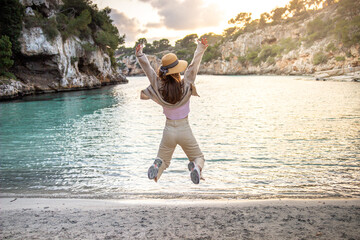 Happy young woman jumping on the beach against the blue water and sunset. Summer holiday concept