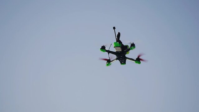 A drone with a camera is spinning in the air against the blue sky. Close-up of the drone