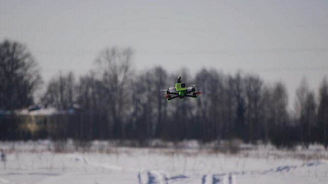 The camera shoots a quadcopter smoothly flying towards the camera on a winter field