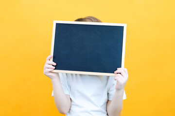 girl holding a board sheet. Cute little girl with chalk board. yellow background. copy space