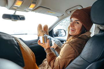 Beautiful young woman wearing warm clothes sitting in car while winter road trip