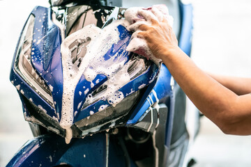 Biker washing scooter . Cleaning motorcycle with sponge or soft cloth at garage , repair and...