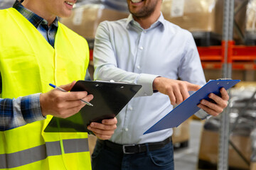 wholesale, logistic business and people concept - close up of manual worker and businessman with clipboards at warehouse