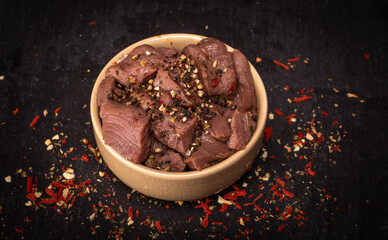 Raw game, beef meat in cubes, in a bowl, on a black background, blackboard. Diced red meat...
