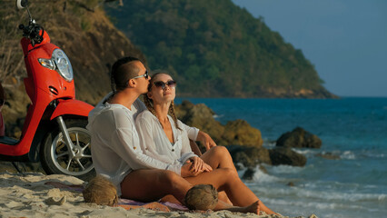 Scooter road trip. Lovely couple on red motorbike in white clothes on sand beach. Just married people kiss hugs walking near the tropical palm trees, sea. Wedding honeymoon by ocean. Motorcycle rent.