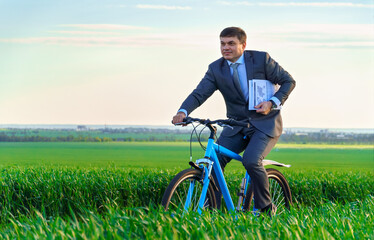 businessman dressed in a business suit, rides with reports or documents a bicycle through a green grass field, beautiful nature in spring, business concept