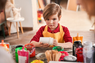 Child boy standing with serious face and holding a lot of plastic cups at the hands