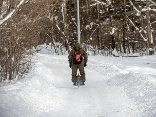 A young man rides a unicycle on a snowy road in the forest.