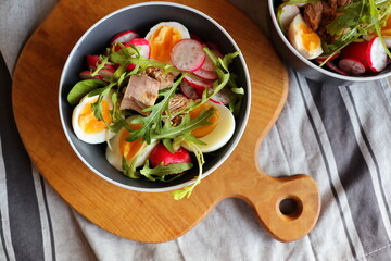 Fresh salad with tuna, radish, eggs, arugula d on gray background top view. Healthy food. Spring salad